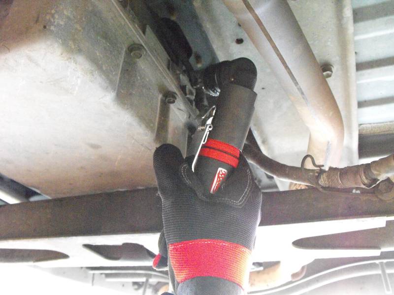 a person wearing gloves and holding a wrench under a vehicle